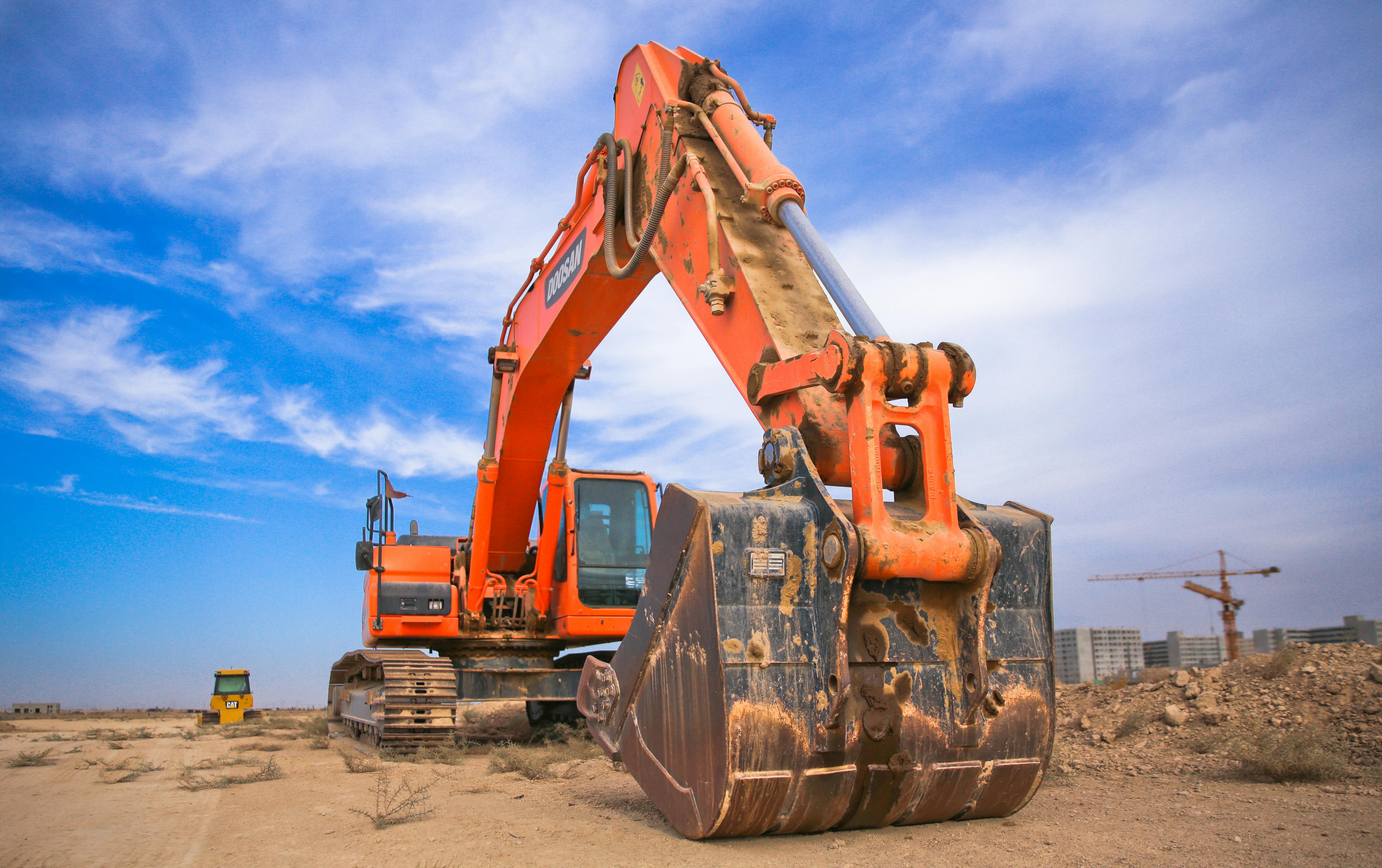 A large orange excavator working on a construction site under a blue sky.